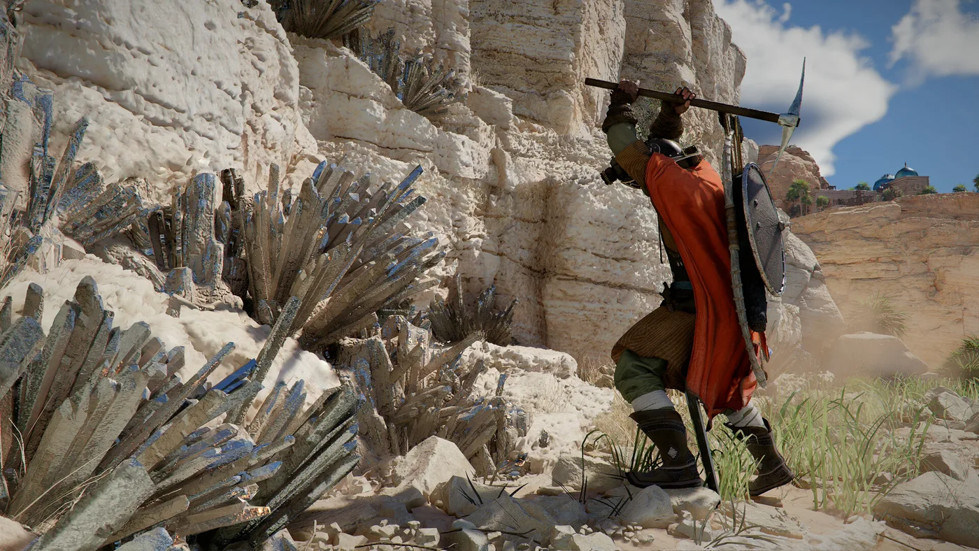 A green-skinned fighter in a dark helmet and an orange cloak, with a round shield and a bow on his back, swings a pickaxe at a pale cliff face studded with dark crystals under a blue sky in Crimson Desert