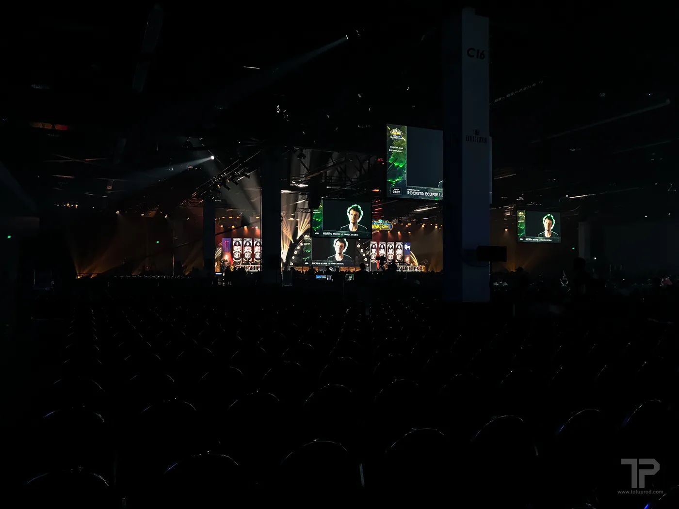 A dark BlizzCon esports hall with large overhead screens displaying "ROCKETS: ECLIPSE 1:2 PANDA GLOBAL" above a lit stage, rows of empty seats in the foreground.