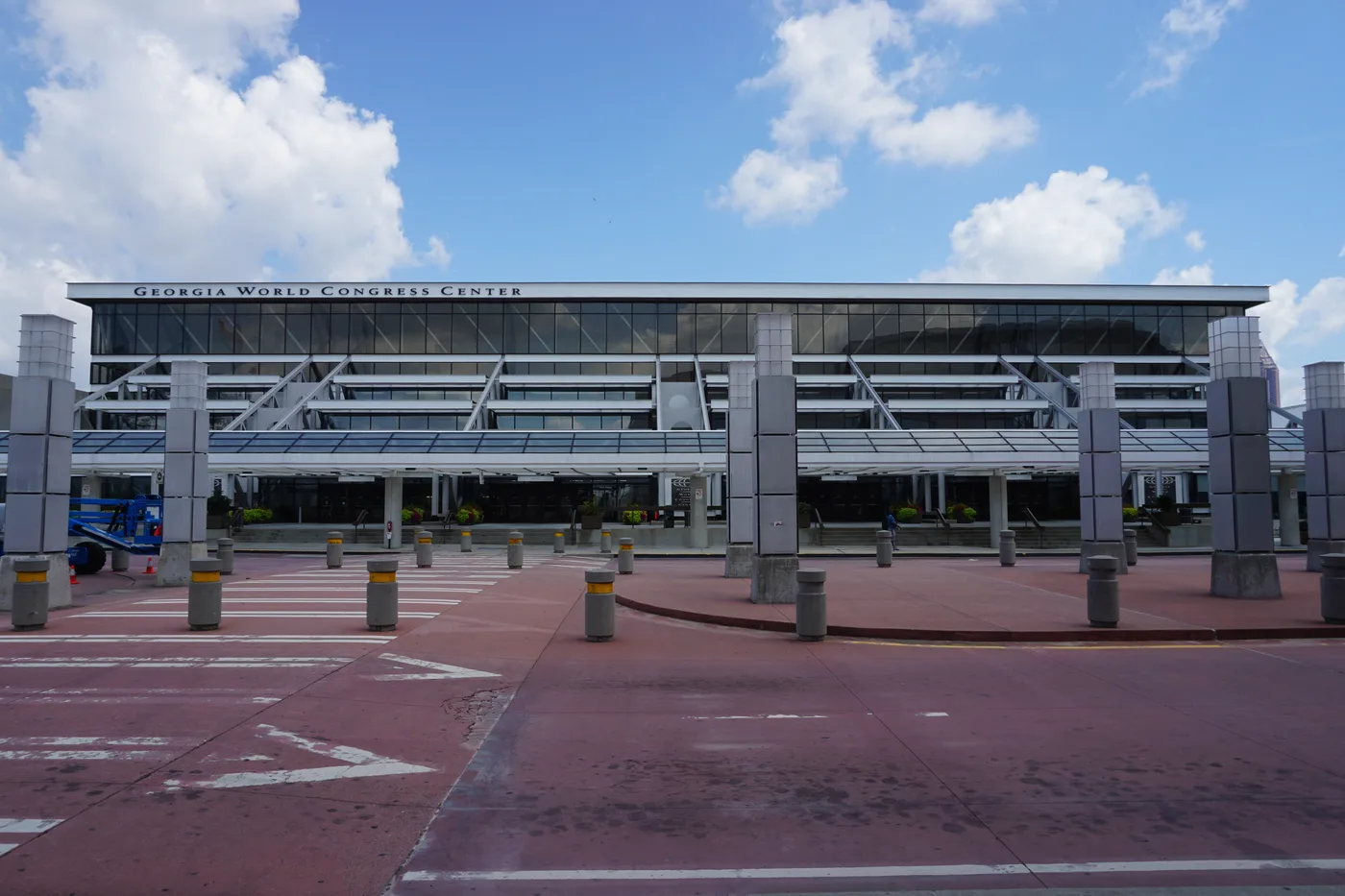 The Georgia World Congress Center in Atlanta seen head-on from its red-paved forecourt: a long glass-and-steel facade with the building name lettered across a white band above the entrance canopy, under a blue sky with scattered cloud.