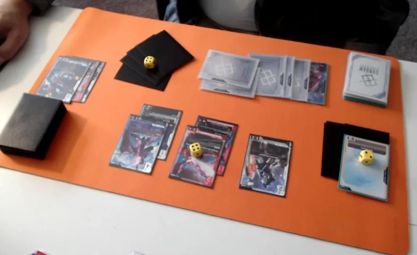 A photo from Bandai's Tournament Rules Manual showing an incorrect webcam setup on the same orange playmat: the Shields sit in a loose black-sleeved pile behind the EX Base on the right, with no clear count and no clear top or bottom card, while a second small black pile with a die sits near the top left.