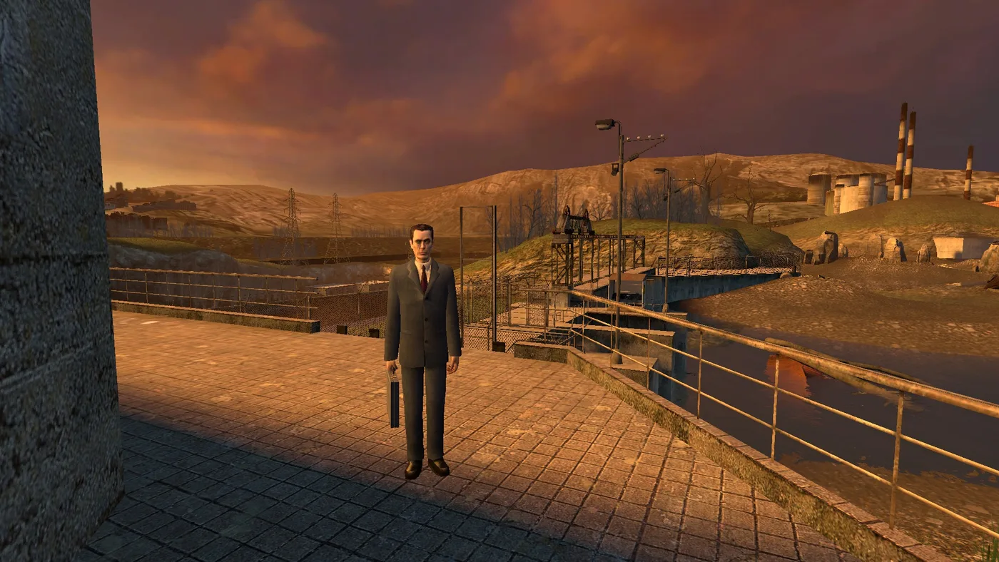 The G-Man standing alone on a paved walkway by a railing at the Water Hazard dam under an orange evening sky, power pylons and smokestacks on the hills behind him.