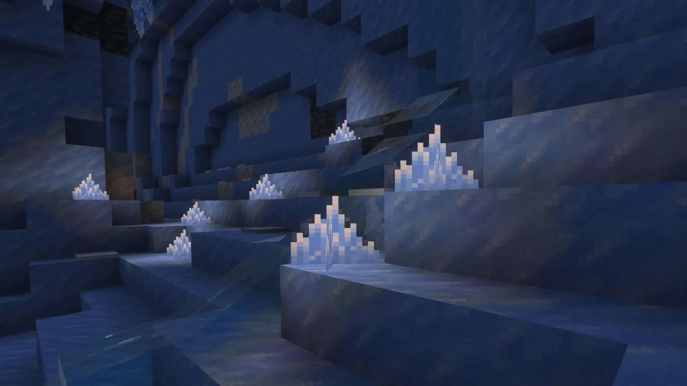 Clusters of white-blue ice crystals sitting on ledges of blue packed ice inside a Minecraft ice cave, with patches of stone and deepslate showing in the wall behind them.
