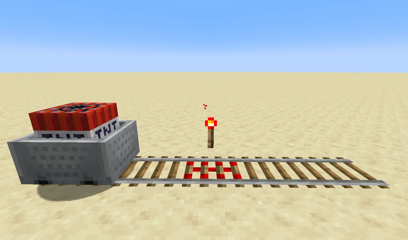 A TNT minecart sitting on a rail line in a Minecraft desert, with a lit redstone torch beside the track powering a glowing red activator rail section.