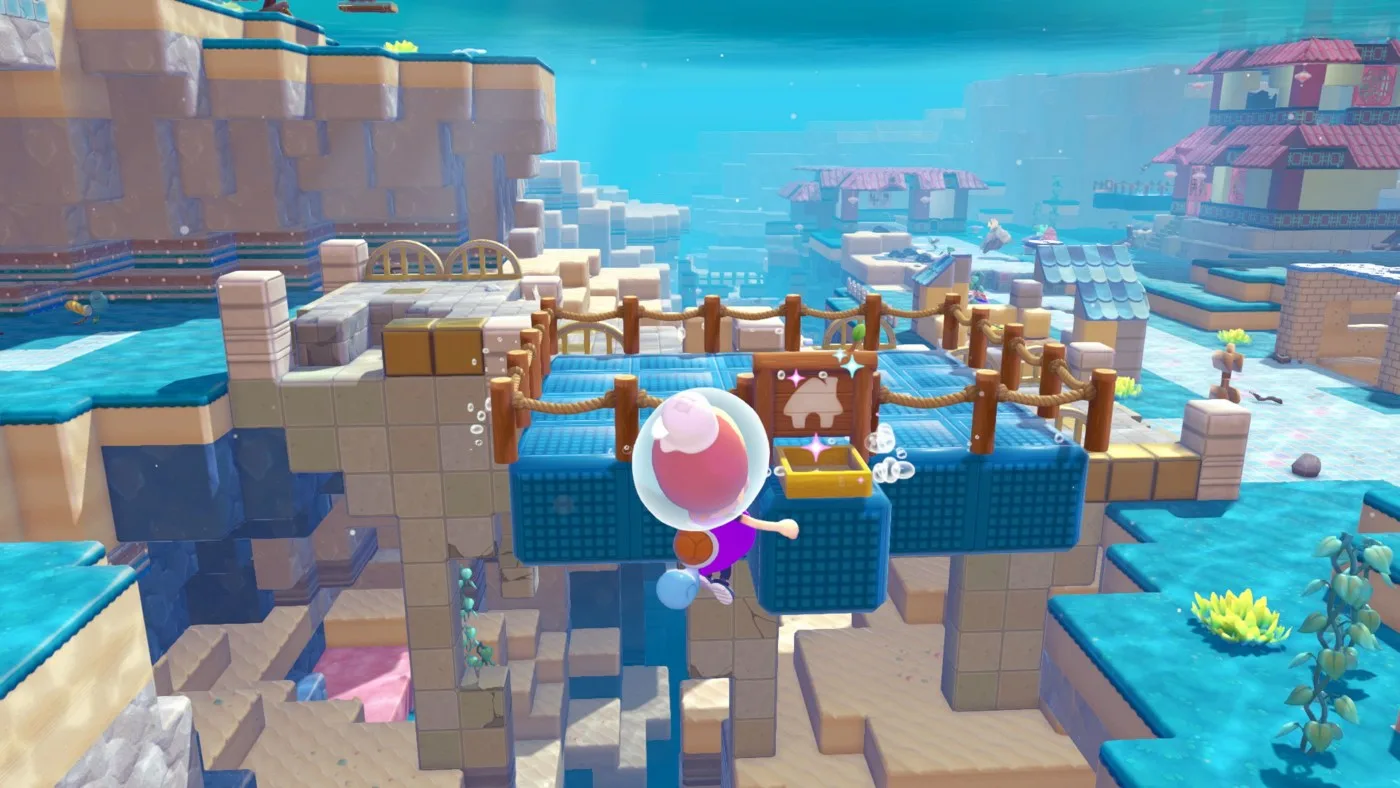 Ditto in human form wearing a bubble helmet places a building kit on floating blue blocks above an underwater Pokopia town with tiled roofs in the distance.