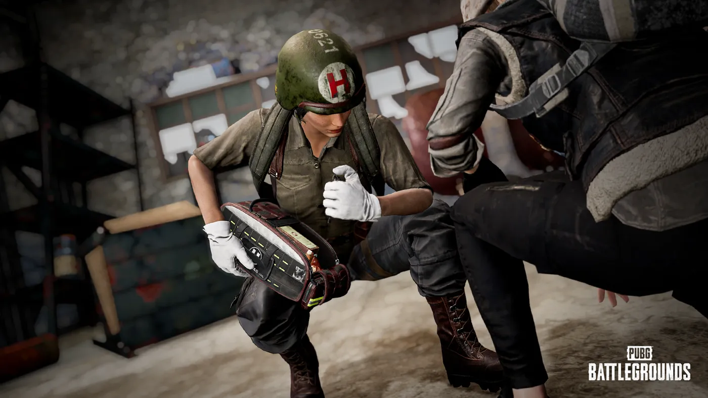 A PUBG player in a medic helmet opening the EMT trauma bag beside a crouched teammate indoors.