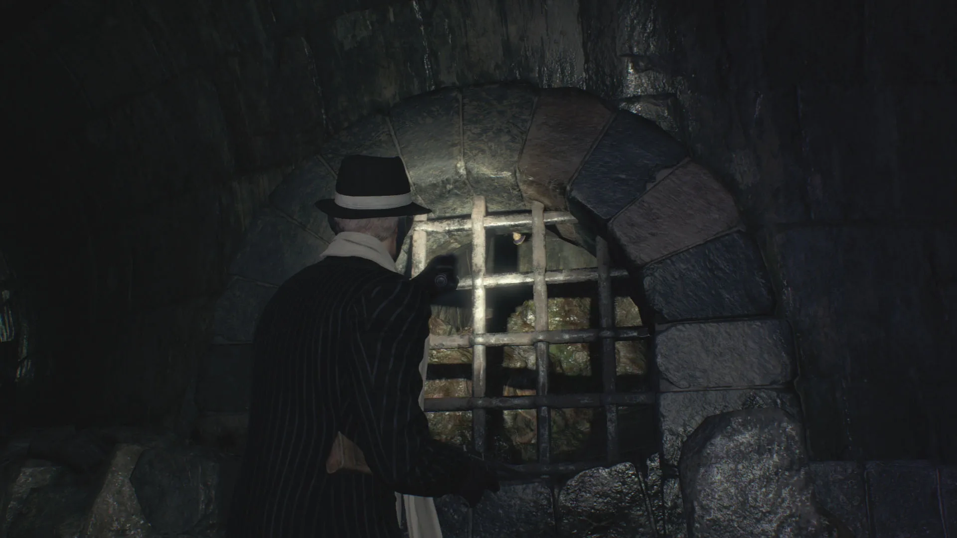 Leon shining a flashlight on the arched wall grate in the Depths that hides the Chapter 10 Clockwork Castellan, across from the sewer Merchant room.