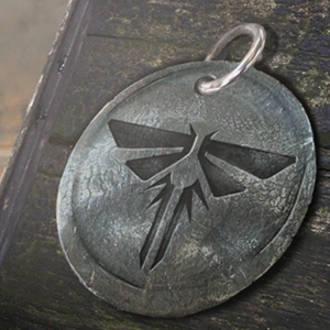 A Firefly pendant collectible held up in The Last of Us Part I, a dog tag belonging to a fallen member of the Fireflies.