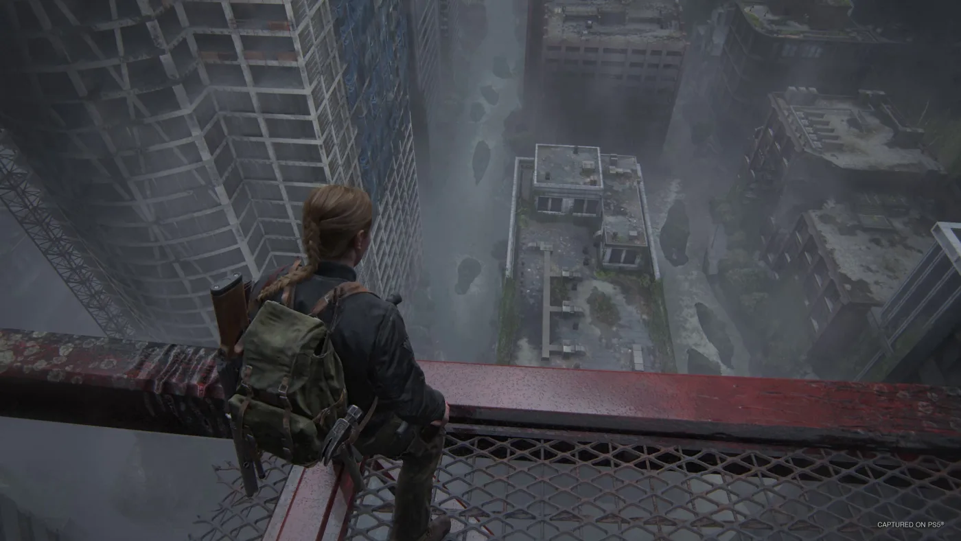 Abby, her braid down her back and a long gun and a hammer strapped to her backpack, crouches at the rail of a red steel skybridge high above fog-filled, overgrown Seattle streets in The Last of Us Part II Remastered.