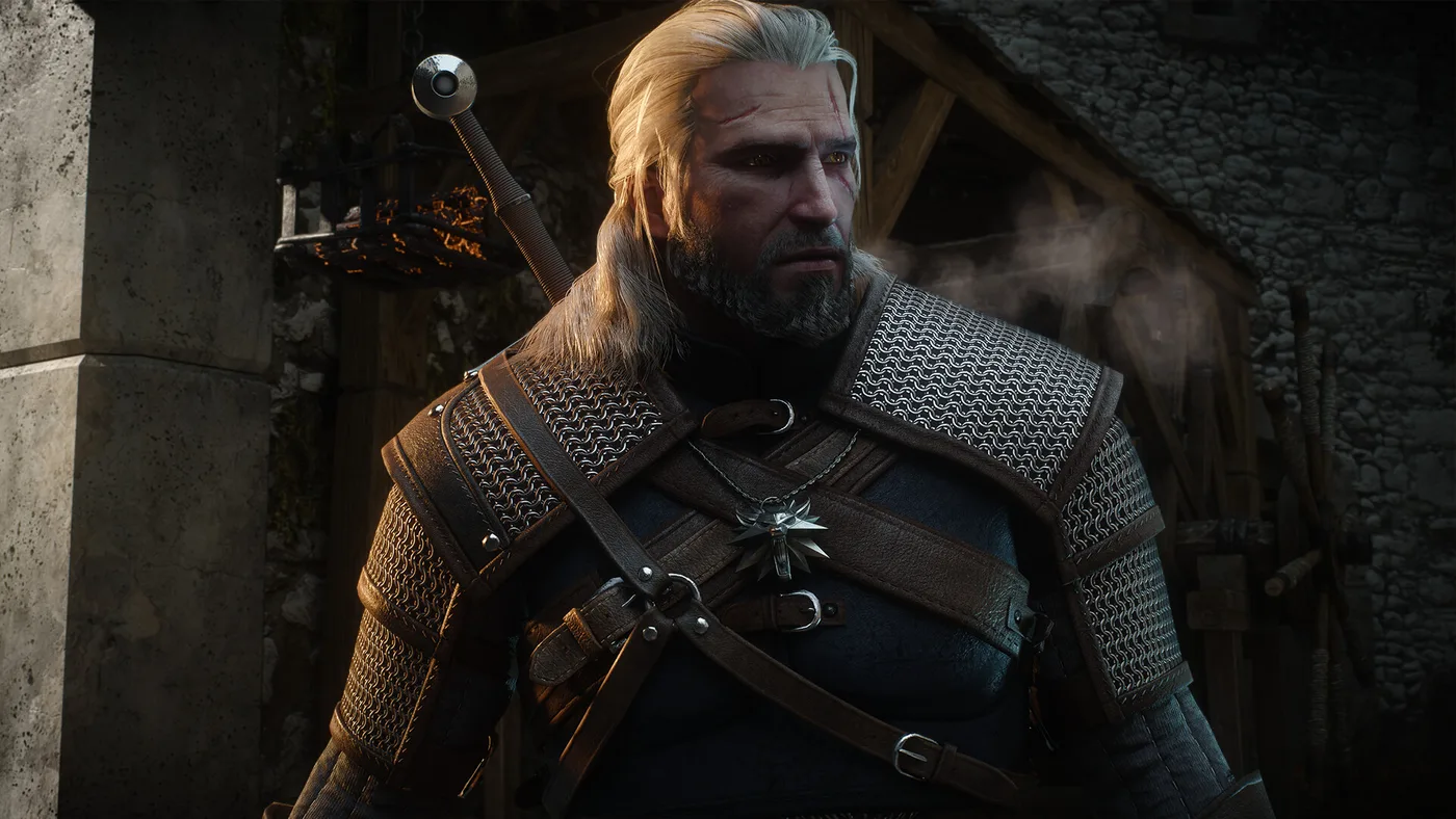 Geralt in close-up in a chainmail-and-leather witcher jacket with his wolf medallion, white hair tied back, a grey beard and a sword hilt over his shoulder, standing beside a stone pillar in front of a dim timber-and-stone building with vapour drifting behind him.