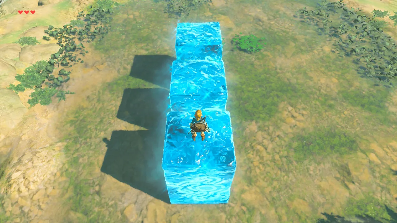 Overhead view of Link standing on the nearest of three blue Cryonis ice blocks raised in a row in Breath of the Wild, their shadows falling across grass and rocks.